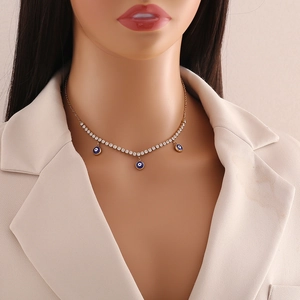 Detailed view of a gold tennis chain necklace with blue evil eye pendants on a model