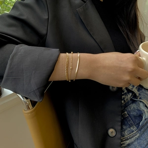 Close-up of three-piece gold snake and cuban link chain bracelet set on female wrist
