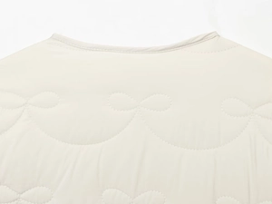 Close-up of wavy quilted stitching and premium padded fabric on cream white jacket