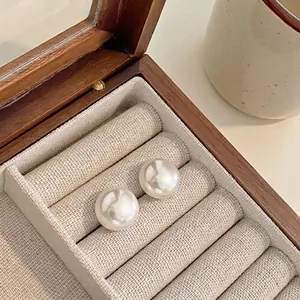 Detail macro view of large white round pearl stud earrings in a wooden jewelry box