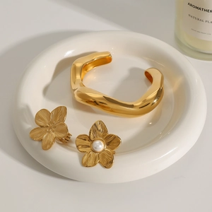 Detailed view of a gold wavy open bangle and floral earrings with pearls on a white tray