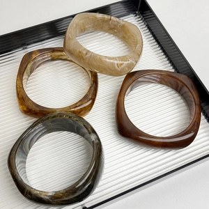 Stack of four geometric resin bangles in marble brown and beige on a striped tray