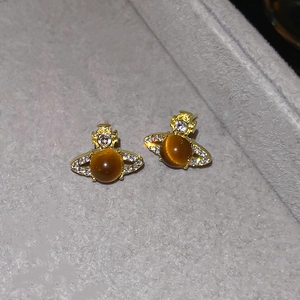 Macro shot of gold-plated Saturn stud earrings with amber cat eye stone and tiny crystals