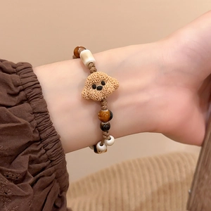 Close-up of handmade woven bracelet with brown teddy dog charm and tiger eye beads