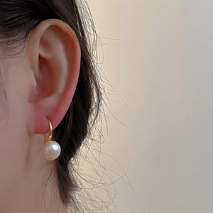 Macro shot of a minimalist gold hook earring featuring a round white freshwater pearl detail