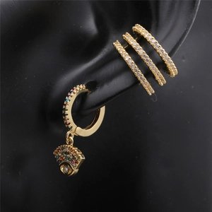 Detailed close-up of golden hoop earring with eye pendant and crystal ear cuffs on black ear model