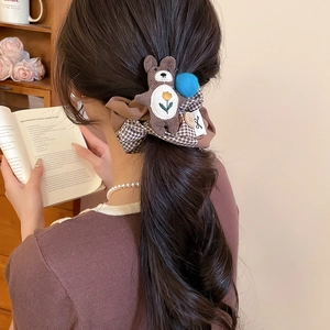Detail of a brown plaid scrunchie with cute knit bear and blue pom-poms on a ponytail