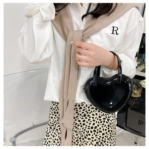 Detailed view of black heart-shaped handbag with glossy finish worn with chic outfit