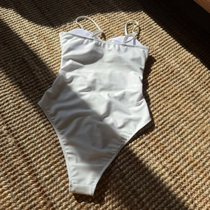 Maillot de bain blanc minimaliste posé à plat sur un tapis tissé texturé