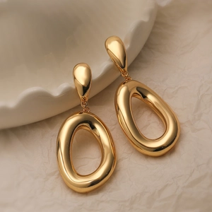 Elegant gold plated geometric oval drop earrings on a minimalist ceramic display base
