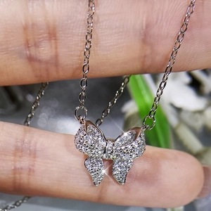 Macro detail of silver butterfly pendant with sparkling zircons on fingertip
