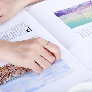 Close-up of three minimalist silver stackable rings worn on a hand over a magazine