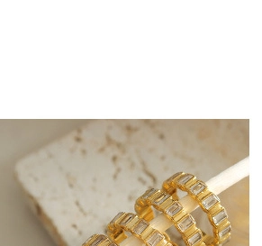 Detail of three gold rings with rectangular clear crystals on marble background