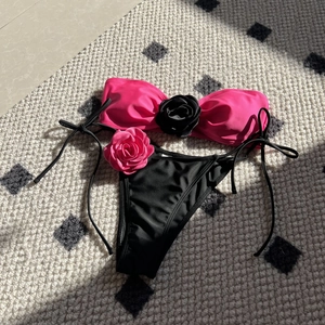 Flat lay of rose pink and black bikini set with 3D handmade floral details and side ties
