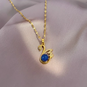 Elegant gold swan necklace with blue stone and clear zircon stones on silk fabric