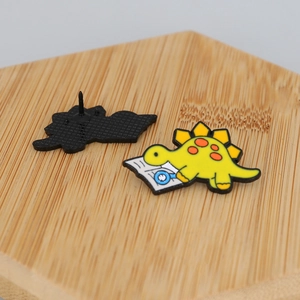 Detail showing the front and back of a yellow cartoon dinosaur enamel pin on a wooden surface