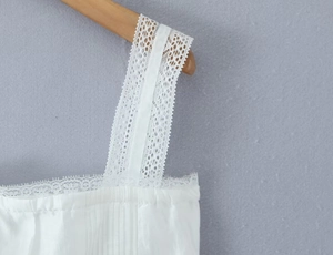 Close-up of elegant white lace shoulder straps and pleated fabric on a wooden hanger