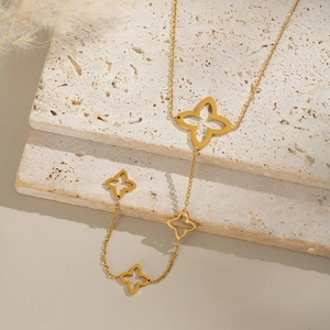 Detail of a gold-toned necklace with four hollow clover pendants on beige stone slabs
