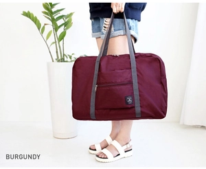 Detail of burgundy foldable travel bag with sturdy grey handles and spacious front pocket
