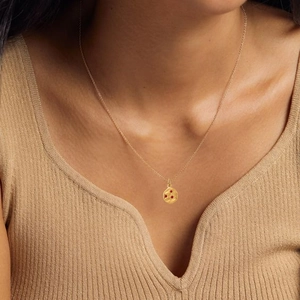 Close-up of a gold necklace with a round red gemstone pendant worn by a model