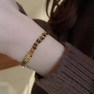 Detail of tiger eye stone beads and gold-toned metal spacers on a woman's wrist