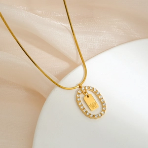 Macro detail of gold oval pendant with zircon halo and letter W on snake chain