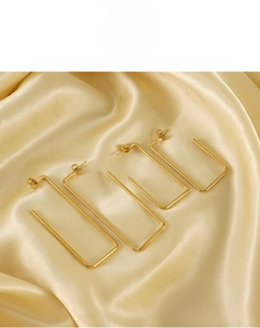 Macro shot of 18K gold-plated geometric square earrings on silk fabric backdrop