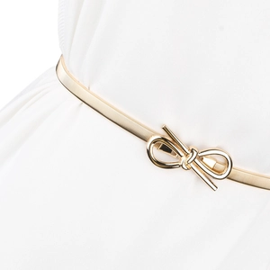 Close-up of a slim golden metal stretch belt with an elegant bow buckle on white fabric