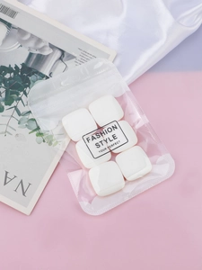Detail view of 6 white square makeup puffs with mesh texture in minimalist packaging