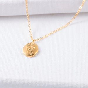 Macro shot of gold rose relief coin pendant with delicate chain on textured cloth