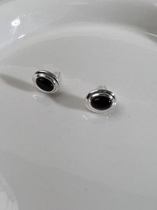 Detail of silver stud earrings with black oval gemstones on a white ceramic plate