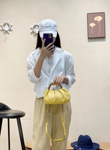 Detail of yellow pleated cloud bag with dark wooden handle and golden chain strap