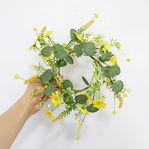 Detail of faux yellow daisies and eucalyptus garland held against a white wall