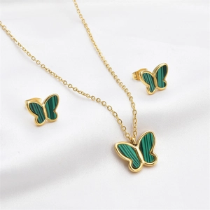 Detailed macro of gold butterfly necklace and earrings set with green stone on silk