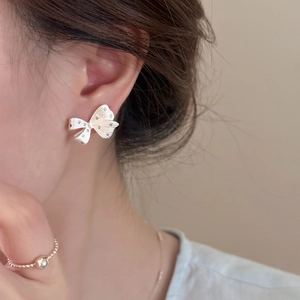 Close-up of a silver bow earring with sparkling diamonds worn by a model