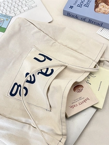 Minimalist cream canvas tote bag with large blue letter print for daily commuting