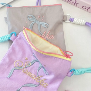 Détail de la broderie nœud et de la bandoulière en corde sur des sacs en toile pastel.