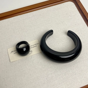 Close-up of chunky black resin open bangle and minimalist bold ring on textured fabric