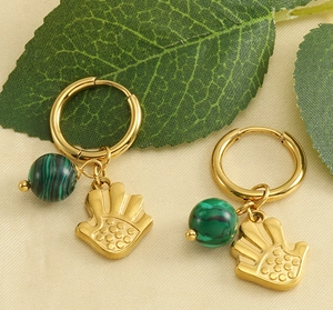 Détail de boucles d'oreilles or 18k avec perles turquoise et charms main de Fatma sur tissu