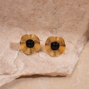Vue détaillée de boucles d'oreilles dorées vintage avec pierre noire sur pierre beige