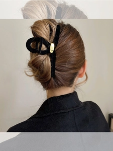 Détail d'une grande pince à cheveux en velours noir avec boucle dorée sur cheveux bruns