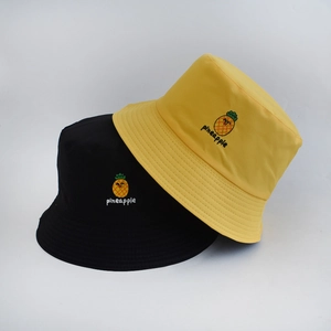 Close-up of yellow and black bucket hats featuring detailed pineapple fruit embroidery