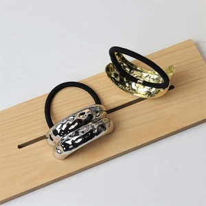 Detail of gold and silver alloy hair ties with hammered metal texture on wooden board