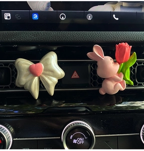 Detail of pink rabbit and white heart car vent clips on a modern vehicle dashboard
