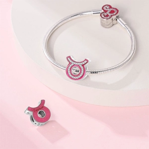 Pink Taurus zodiac charm with silver snake bone bracelet on geometric display bases