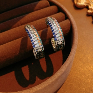 Detailed shot of silver C-shaped earrings with colorful cubic zirconia on brown suede box