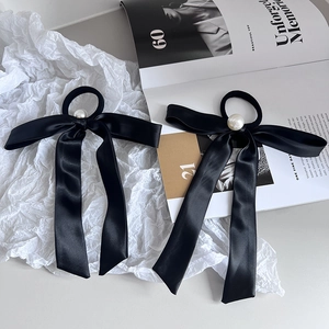 Close-up of elegant black silk bow hair ties with pearl centers on a magazine