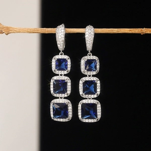 Close-up of three-tier square blue zircon drop earrings with pavé halo on wooden branch
