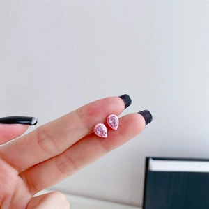 Close-up of pink pear-cut gemstone stud earrings with enamel border held in fingers