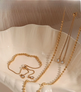 Detail of adjustable golden stainless steel bead necklace and bracelet set with zircons